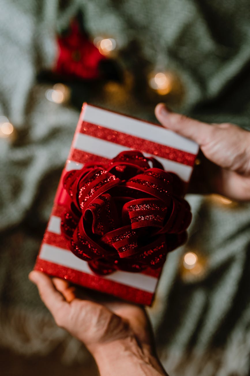 person holding red and white gift box with ribbon bow